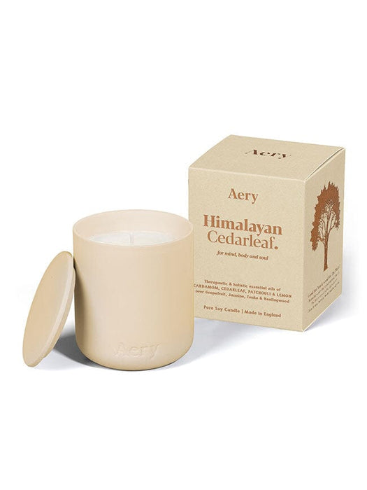 Cream Himalayan Cedarleaf candle by Aery displayed next to product packaging on white bacground 