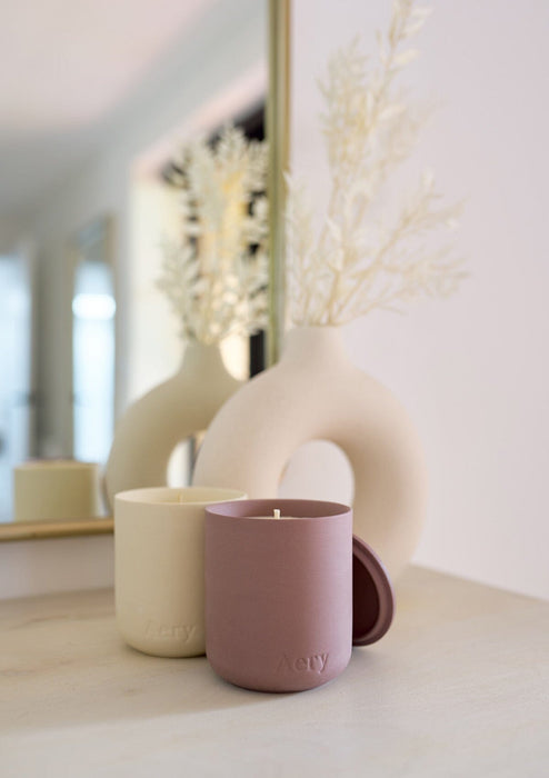 Aubergine moroccan rose candle by aery displayed next to Himalayan candle by aery sat on cream side table 