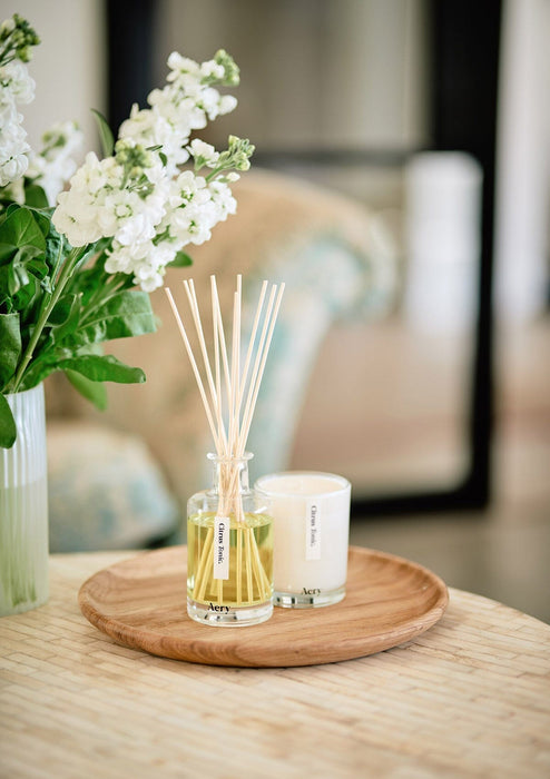 Citrus Tonic diffuser by aery displayed next to citrus tonic candle and vase of white flowers 