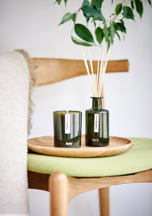 Green Bamboo diffuser by aery displayed next to green bamboo candle by aery placed on wooden tray 