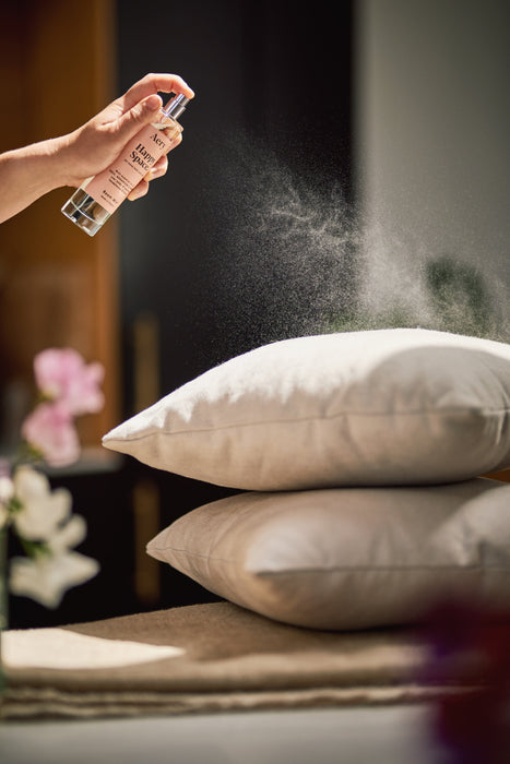 Pink Happy Space room mist by aery displayed in hand spraying onto pillows 